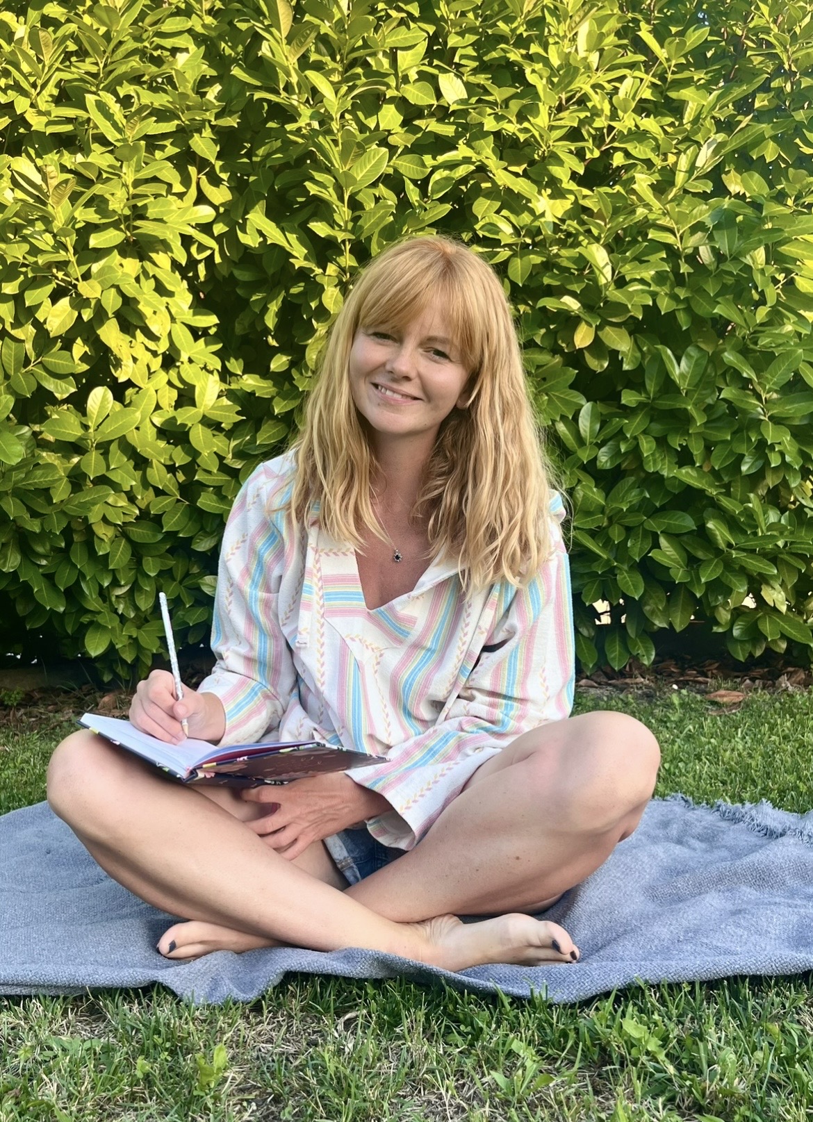 Kasia sitting outdoors in nature, journaling in a peaceful green setting